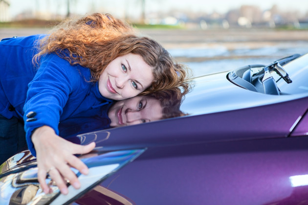 Mujer recostada sobre el cofre de su carro nuevo color morado. 
