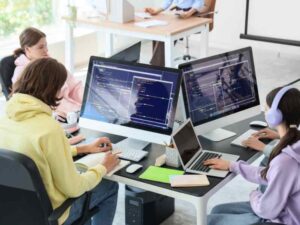 Estudiantes programando en computadoras de escritorio en un aula de tecnología, desarrollando habilidades digitales para empleos de la economía 4.0.